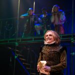 Actor intensely looking at the audience with three actors on a balconey above in the 2019 production of Twelfth Night
