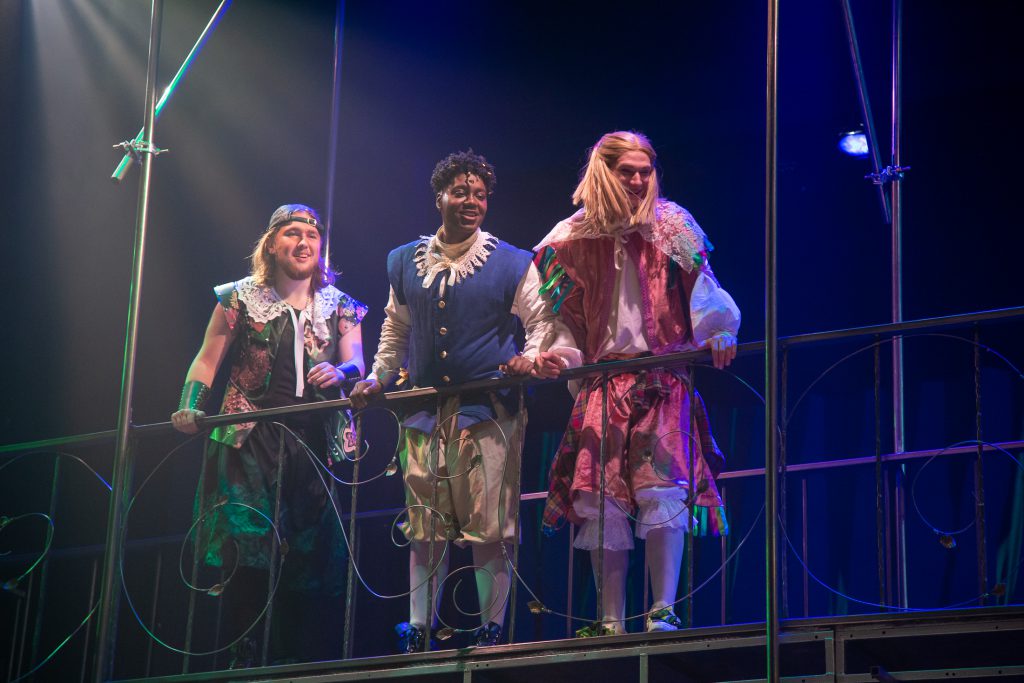 Three actors looking down from a balcony in the 2019 production of Twelfth Night